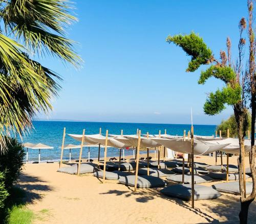 una playa con sombrillas y sillas blancas en la playa en The Bay Hotel & Suites en Vasilikós