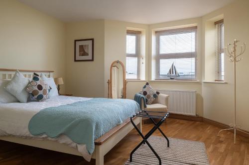 a bedroom with a bed and a chair and windows at Orme View in Llanfairfechan