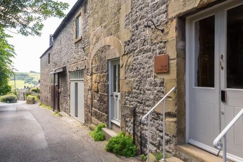 a stone building with a white door on a street at Beautifully Renovated Old Sweet Shop in Youlgreave