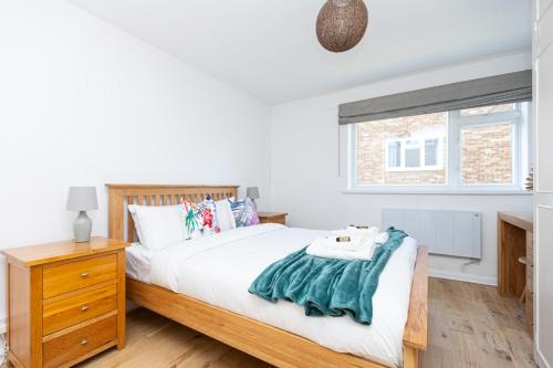 ein Schlafzimmer mit einem Bett, einer Kommode und einem Fenster in der Unterkunft Lit & airy 2BR Flat wparking & balcony, Wimbledon in London