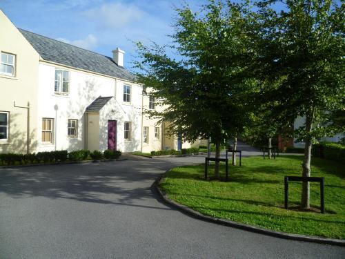 a white house with trees in front of a street at Bunratty Castle Gardens Home in Bunratty