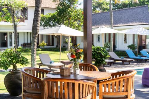 a patio with a wooden table with chairs and umbrellas at BougainVilla - Oceanfront villa with Cook, ideal for Weddings and Events in Keramas