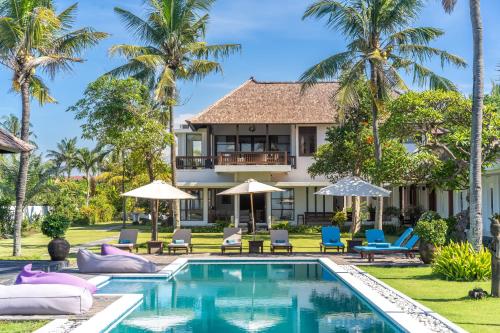 a villa with a swimming pool and palm trees at BougainVilla - Oceanfront villa with Cook, ideal for Weddings and Events in Keramas