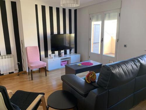 sala de estar con sofá de cuero negro y TV en Precioso ático con garaje gratis en Salamanca