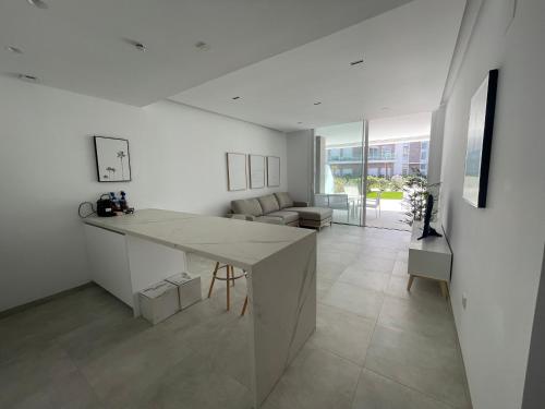 eine weiße Küche mit Tisch und ein Wohnzimmer in der Unterkunft Costa Ballena - Dos dormitorios, Piscina y Jardín privado in Cádiz