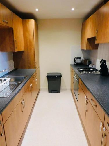a kitchen with wooden cabinets and a trash can at No 2 - Modern 2 Bed Apartment Close to Gla Airport & M8 in Paisley