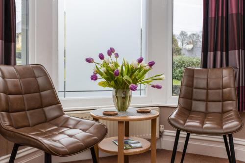 two chairs and a vase with purple flowers on a table at Thornbank House Offering Breakfast and with the use of Free Local Health Club in Windermere