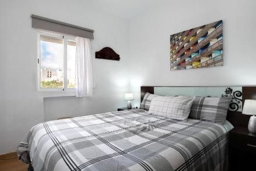 a bedroom with a bed with a plaid blanket and a window at Casa El Muro in Vejer de la Frontera