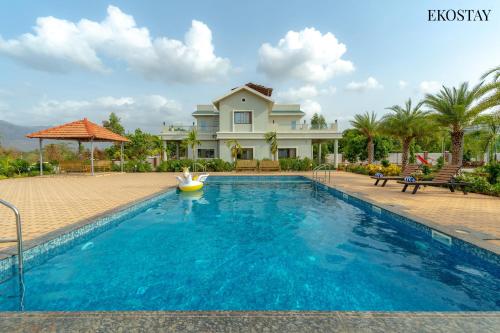a swimming pool in front of a house at Ekostay Gold Palm Estate I Cricket Turf I Rain Dance I 2 Acre Property in Karjat