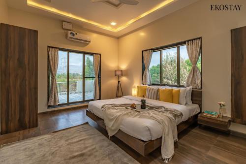 a bedroom with a large bed and two windows at Ekostay Gold Palm Estate I Cricket Turf I Rain Dance I 2 Acre Property in Karjat