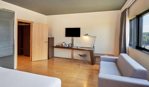 a living room with a couch and a desk with a television at NH Madrid Las Tablas in Madrid