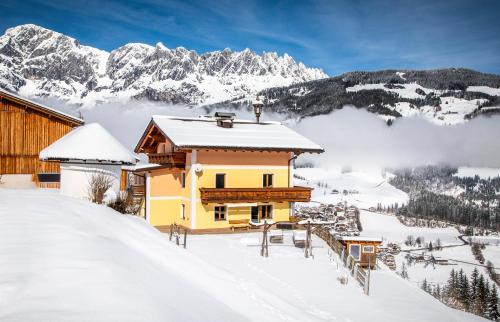 a house in the snow with mountains in the background at Brennergut Ferienwohnung am Bauernhof in Mühlbach am Hochkönig