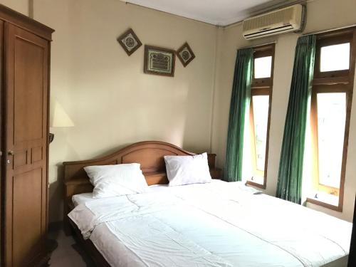 um quarto com uma cama com lençóis brancos e cortinas verdes em Wisma Atma Bhakti RedPartner near Solo Square em Lawean