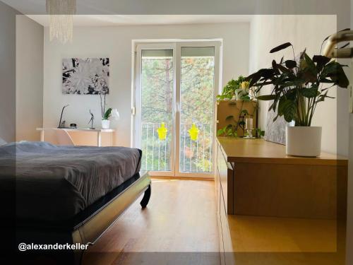 Schönes und ruhiges Privatzimmer mit französischem Balkon في ميونخ: غرفة نوم بسرير ومكتب بالنباتات