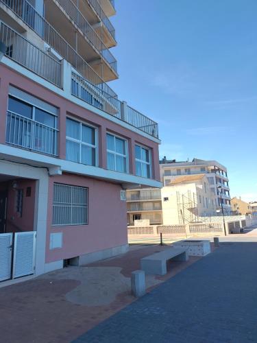 um edifício cor-de-rosa com um banco à frente. em Breezy Beach Apartment em Sueca