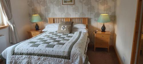 a bedroom with a bed and two night stands with lamps at Ornum Cottage in Beauly