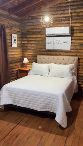 1 dormitorio con cama blanca y pared de madera en Cabañas Los Aires San Vicente en San Vicente