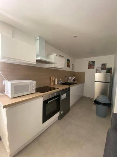 une cuisine avec des armoires blanches et un micro-ondes dans l'établissement Chez Julie petit appartement une chambre rez jardin maison, à Tulle