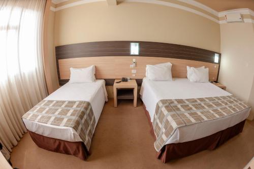 a bedroom with two beds and a table at Hotel Executive Arapongas in Arapongas