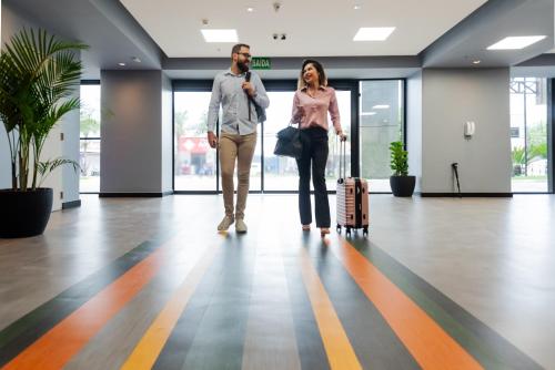 two people walking through an office lobby with their luggage at ibis Styles Goiânia Shopping Estação in Goiânia