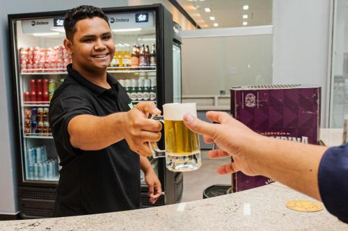 a man is handing a man a glass of beer at ibis Styles Goiânia Shopping Estação in Goiânia