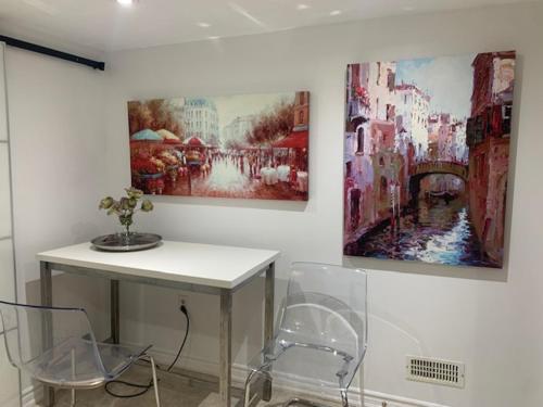 a table with two chairs and two paintings on a wall at Cosy comfortable basement apartment. in Toronto