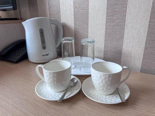 two cups and saucers on a table with a coffee maker at All-in rooms in Vilnius