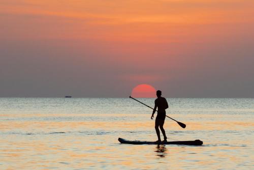 a man standing on a paddle board in the ocean at Sunset Sanato Resort & Villas in Phu Quoc