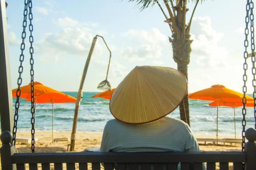 a person wearing a hat sitting on a swing at the beach at Sunset Sanato Resort & Villas in Phu Quoc