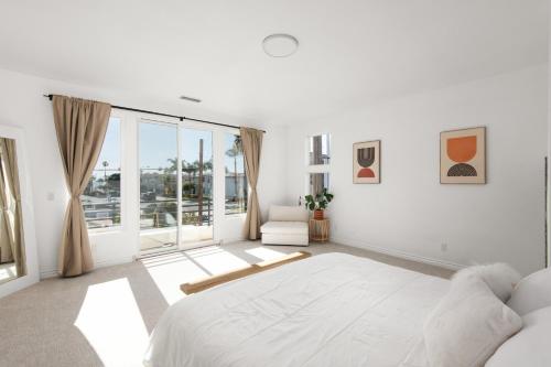 a white bedroom with a large bed and a large window at Modern beach home with rooftop - Ocean View! in Oceanside