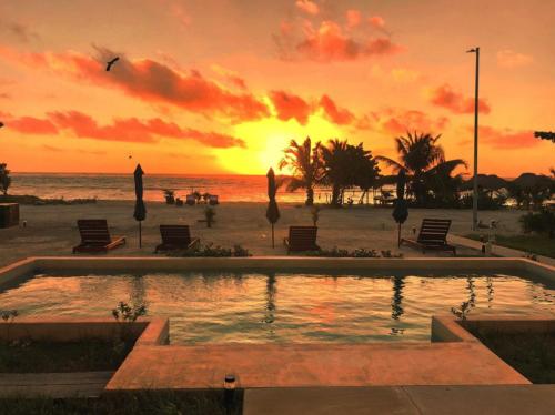 una piscina en la playa con una puesta de sol en el fondo en Condos Azul Azul Mahahual, en Mahahual