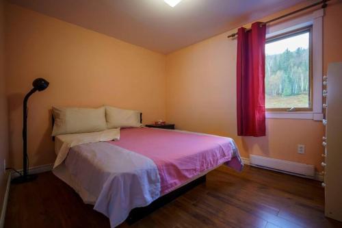 a bedroom with a bed with a pink blanket and a window at Le Remous in La Malbaie