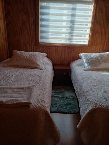 2 camas individuales en una habitación con ventana en Cabañas Carmencita, en Puerto Puyuhuapi
