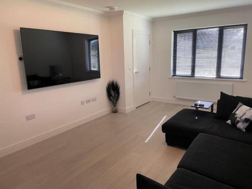 Modern 2 Bedroom House, Edinburgh. في Millerhill: غرفة معيشة مع أريكة سوداء وتلفزيون بشاشة مسطحة