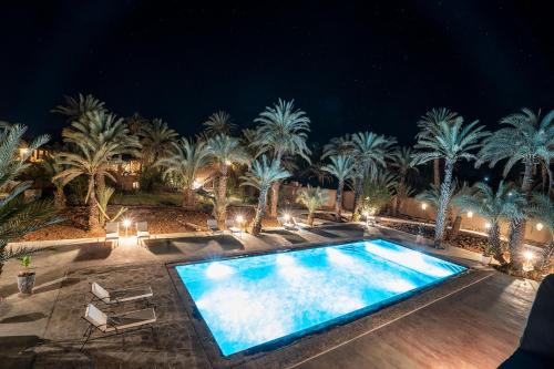 a swimming pool in front of palm trees at night at Lodge Hara Oasis in Agdz