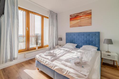 łóżko z niebieskim zagłówkiem w pokoju z oknami w obiekcie 3L Apartments Olympic Park w Kołobrzegu