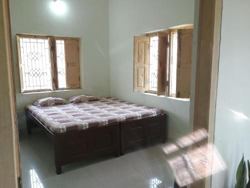 uma pequena cama num quarto com duas janelas em Budha ashram guest house em Bodh Gaya