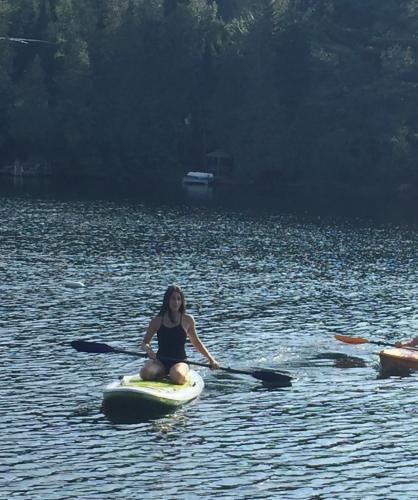 a woman sitting on a paddle board in the water at Winter Lakefront Chalet - Serendipity Hideaway - Ski, Skate, Snowshoes & Relax by the Cozy Fire in Chertsey