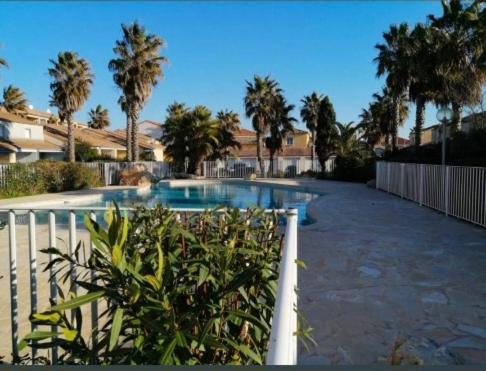 une piscine avec des palmiers et une clôture dans l'établissement Plume, à Valras-Plage