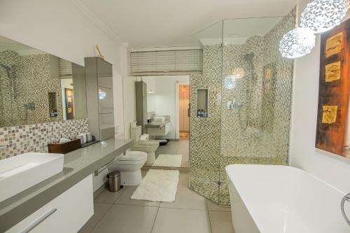 Belvedere Boutiqe Hotel في ويندهوك: حمام فيه مغسلتين ودش ودورتين مياه