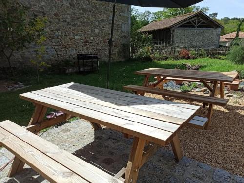 two wooden picnic tables in a yard with an umbrella at Gite 3 chambres, 2 à 10 pers et jardin clôturé in Oradour-sur-Glane