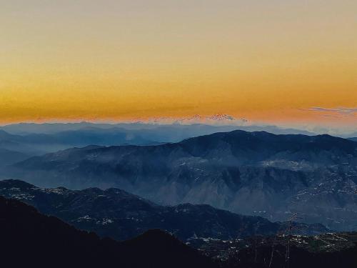 a view of a mountain range with clouds in the sky at Maayaa Ridge House in Kanatal
