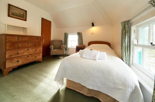 a bedroom with a white bed and a dresser and a window at Portmeirion Village & Castell Deudraeth in Porthmadog