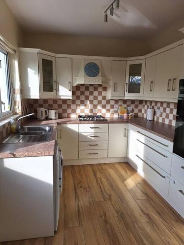 a kitchen with white cabinets and a wooden floor at 'Grange Hideaway' Town Centre (Sleeps 6) in Omagh