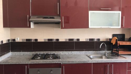 een keuken met rode kasten, een wastafel en een fornuis bij شقة لقضاء عطلة مميزة بمدينة الفنيدق in Riffiene