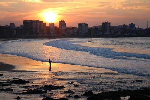 希洪的住宿－EL ENCANTO CON VISTAS PARKING PRIVADO，日落时站在海滩上的人
