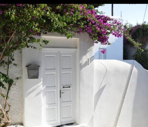 a white door in a white wall with purple flowers at Kamara Residence & Suites in Mikonos