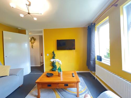 uma sala de estar com paredes amarelas e uma mesa de centro em 1BR Flat MK Centre - Free Parking - Private Garden - Long stays welcome - just ask em Milton Keynes