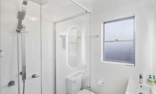 a white bathroom with a shower and a mirror at Sand and Sea 1 - Opposite Sawtell's Main Beach & Steps to Cafes, Restaurants & Boutiques! in Sawtell