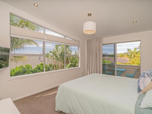 Acacia Cote - Whitianga Holiday Home في وايتيانغا: غرفة نوم بسرير ونوافذ كبيرة